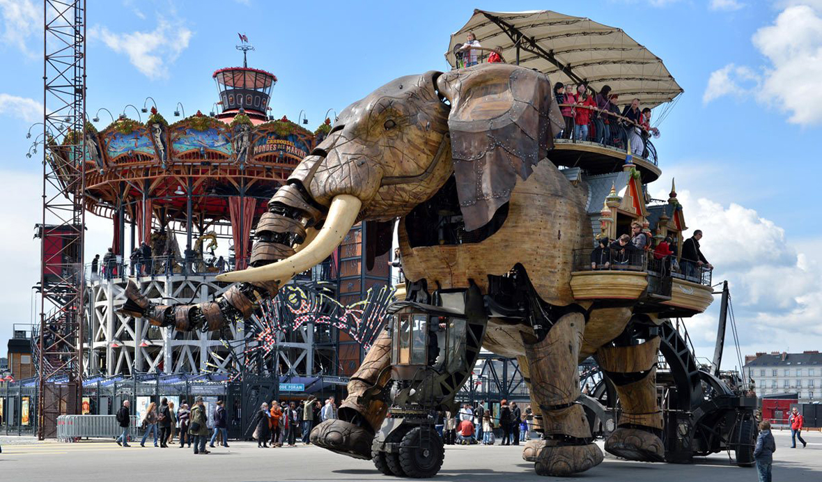Mechanical elephant walking past a carousel with people riding on its back and sides